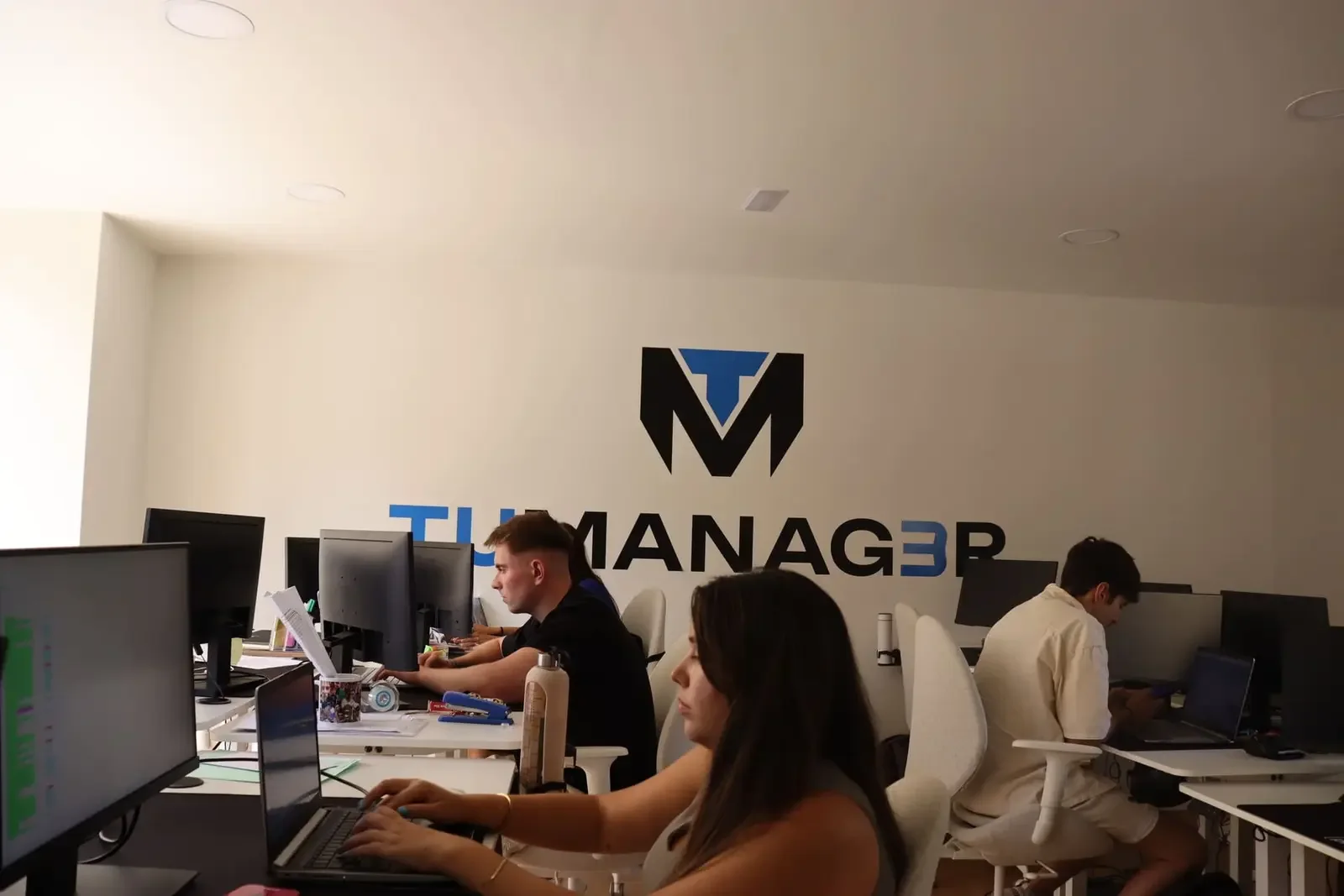 Part of the team working at their desks under the TuManag3r logo