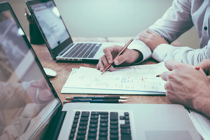 Dos personas revisan anotaciones en una mesa con ordenadores portátiles