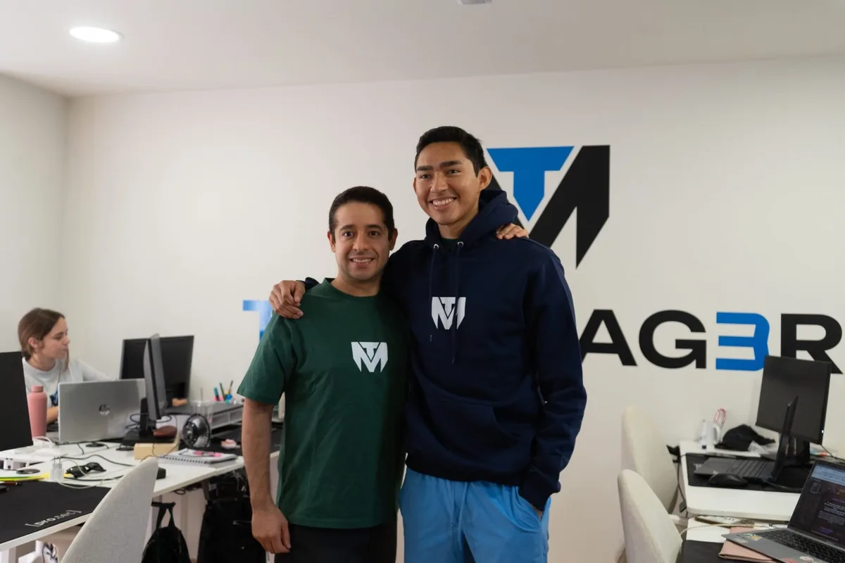 Two men in TuManag3r clothing pose in the office