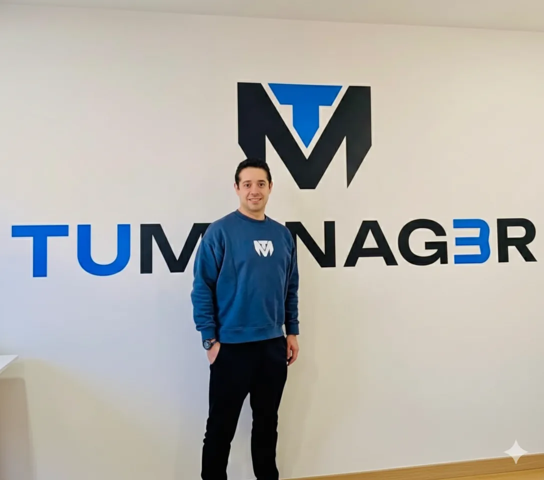 Man wearing a blue sweatshirt in front of the TuManag3r logo