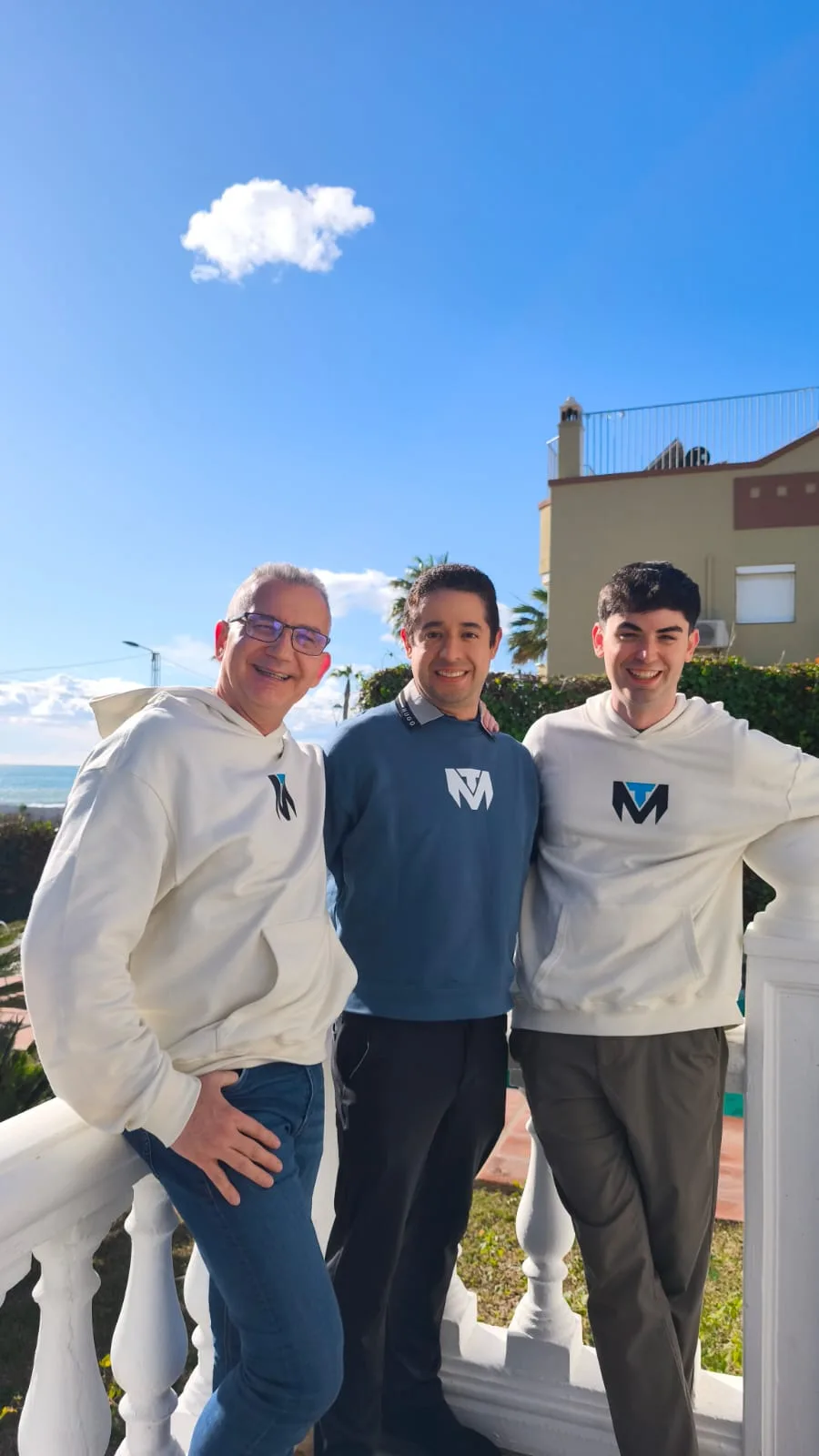 Three men wearing TuManag3r clothing pose on a terrace by the sea