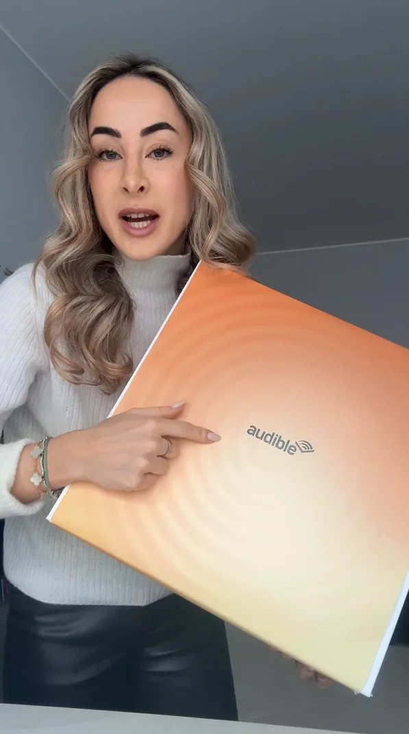 Una mujer muestra ante la cámara una caja con el logotipo de Audible
