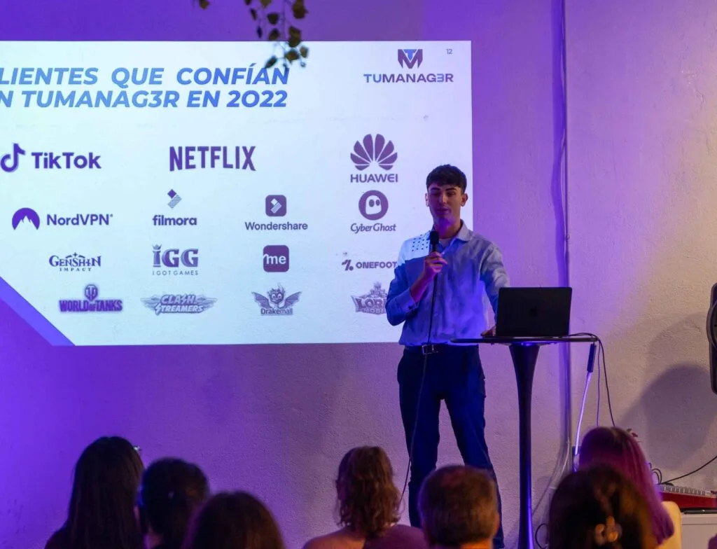 A speaker with a microphone presents in front of a slide of brands