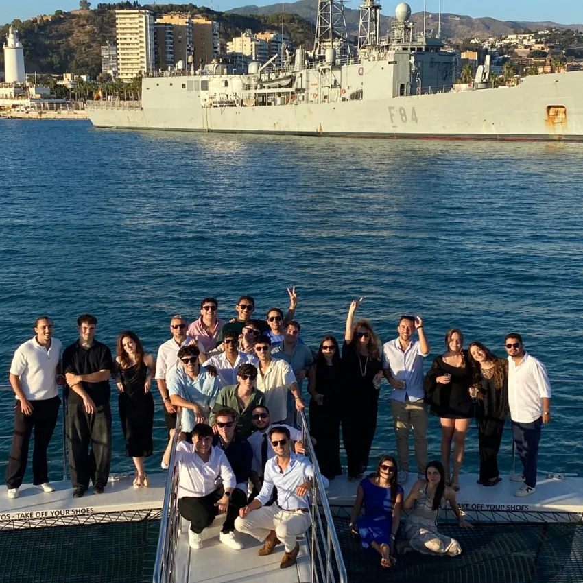 Group of people on a boat with a ship in the harbour behind them